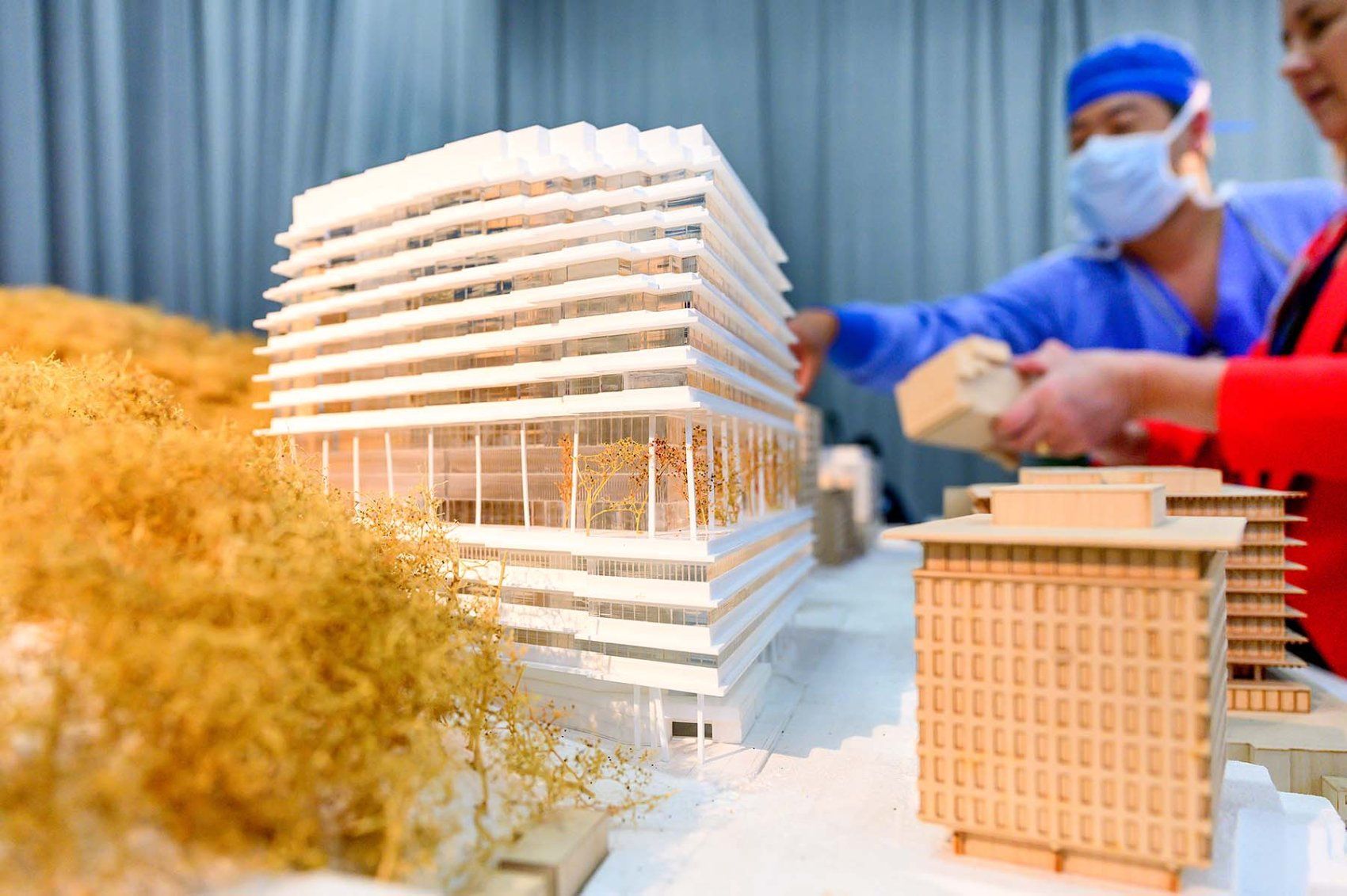 Les visiteurs interagissent avec une maquette du nouveau bâtiment de l'hôpital, complétée par de petits arbres contre le mont Sutro.