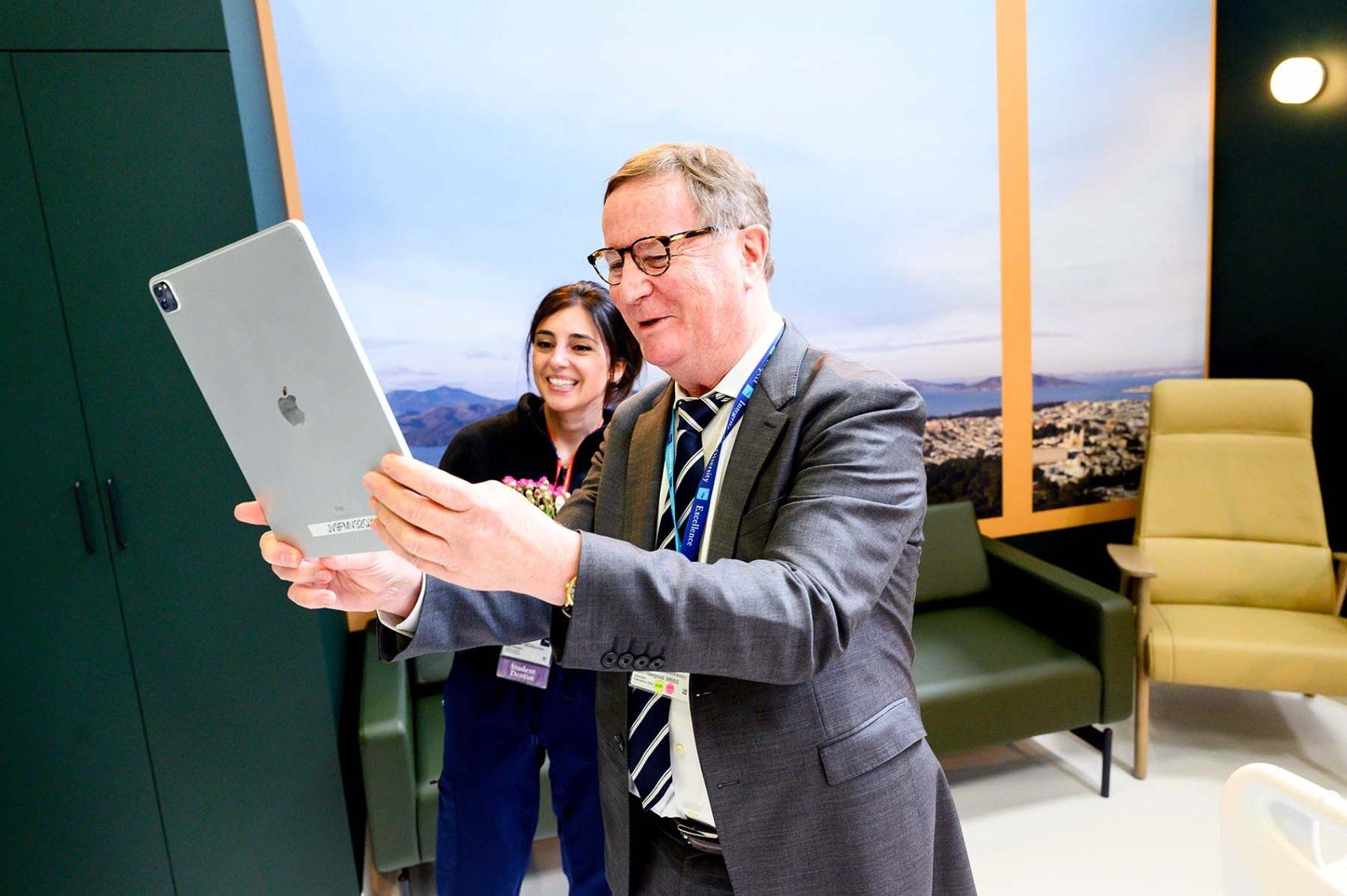 Le chancelier de l'UCSF, Sam Hawgood, MBBS, rit avec un participant alors qu'il brandit un iPad pour explorer une expérience de soins aux patients en réalité augmentée.