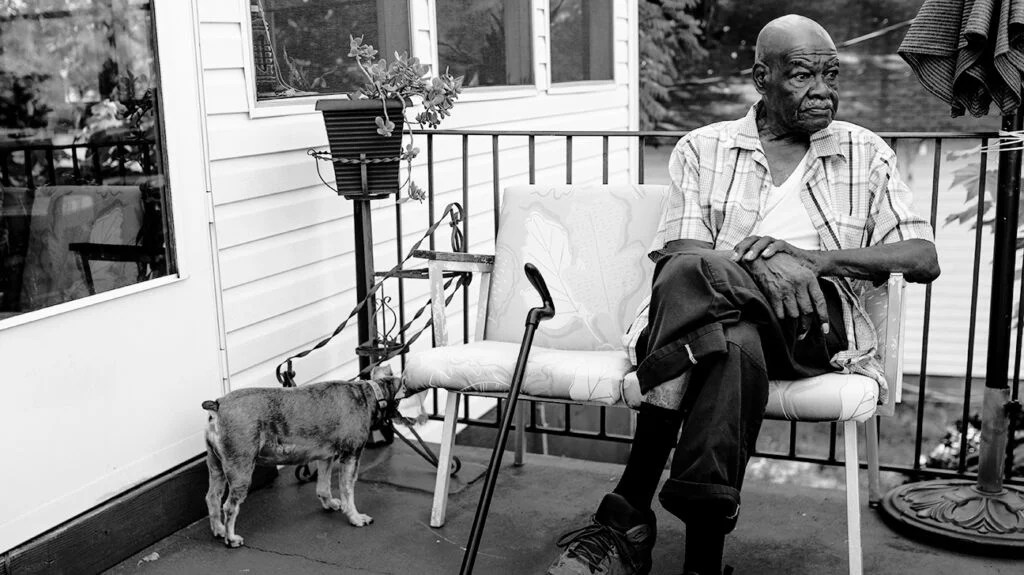 Un homme plus âgé avec une canne et un chien est assis sur un porche