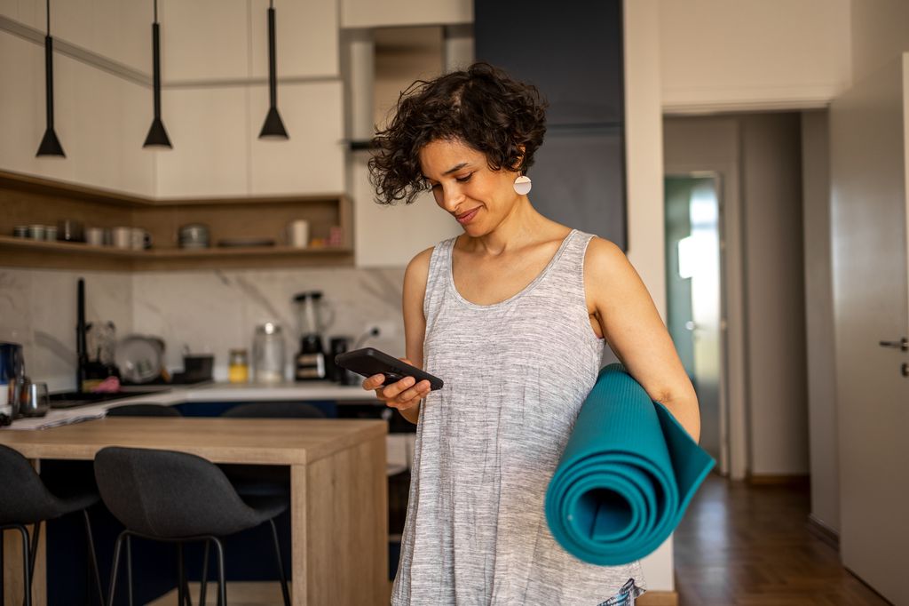 Femme se préparant à la pratique du yoga, elle utilise son téléphone portable pour trouver de la musique adaptée