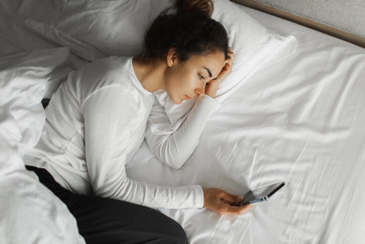 Femme allongée dans son lit et parcourant les médias sociaux.