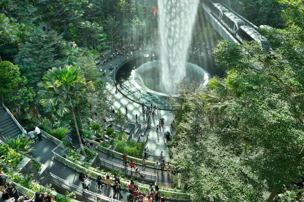 Une vue aérienne de voyageurs internationaux rassemblés autour de la cascade intérieure, presque cachée dans la verdure de l'aéroport Jewel Changi.