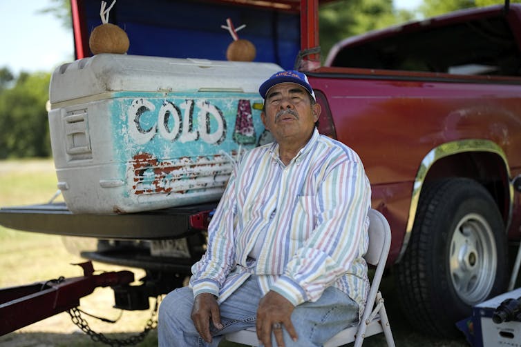 Un homme est assis sur une chaise et ferme les yeux à côté d'une glacière à l'arrière d'un camion.