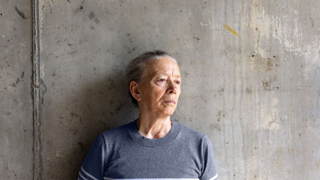 Une femme plus âgée et pensive se tient contre un mur gris