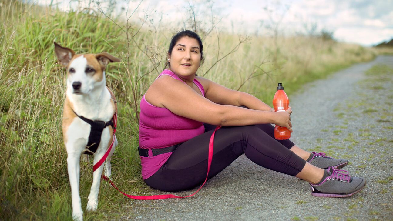 Une femme en tenue de sport fait une pause sur une route à côté d'un chien blanc et marron.