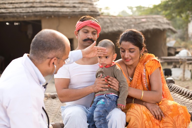 Un petit garçon est assis sur les genoux de ses parents pendant qu'il est examiné par un médecin, dans un village rural