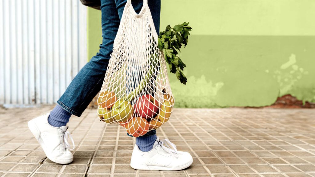 Une personne tenant un sac de fruits et légumes frais marche sur un trottoir