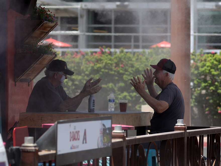 Les gens discutent en prenant un verre sous un monsieur dans un restaurant de Phoenix mercredi.  Selon le National Weather Service, Phoenix connaîtra des températures record dépassant les 100 degrés en raison d'un dôme thermique provenant de la haute pression atmosphérique. 
